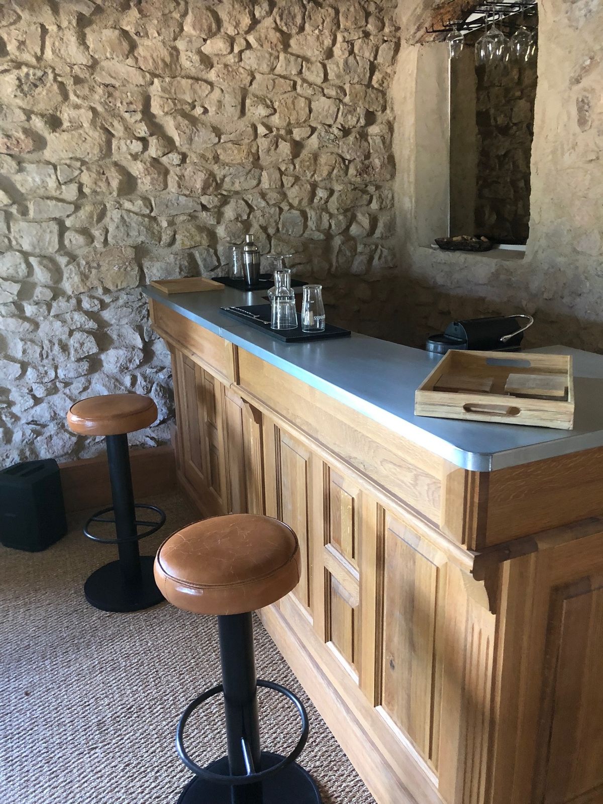 The wooden bar and its stools, set against a stone wall.