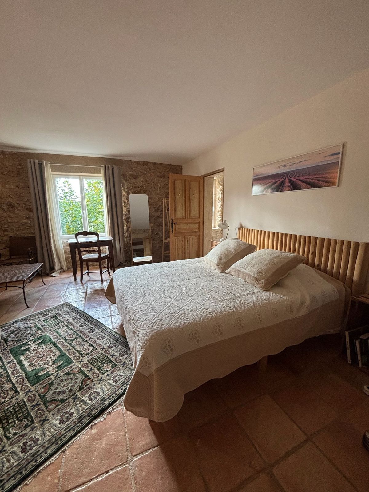 Room 1: the bed, the desk by the window and a rug on the terracotta floor.