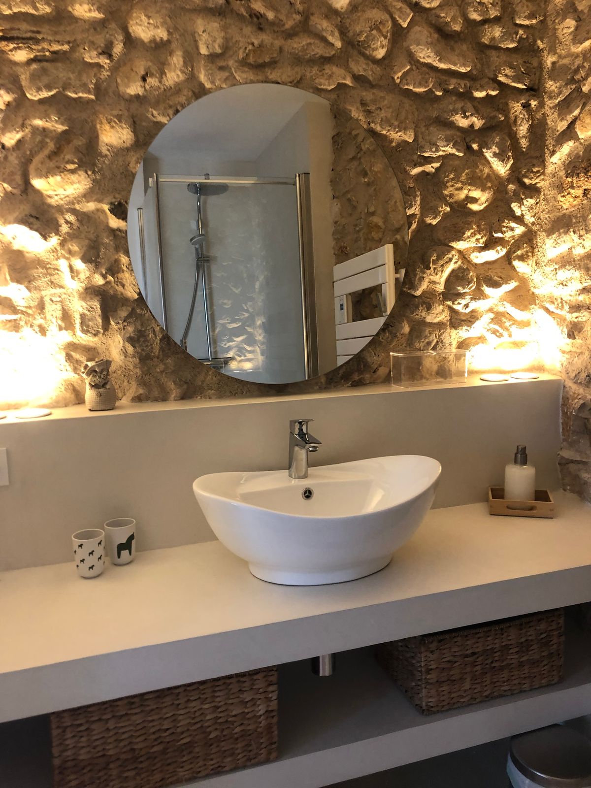 Room 3’s shower room: a basin on a white counter and a round mirror, against a lit stone wall.