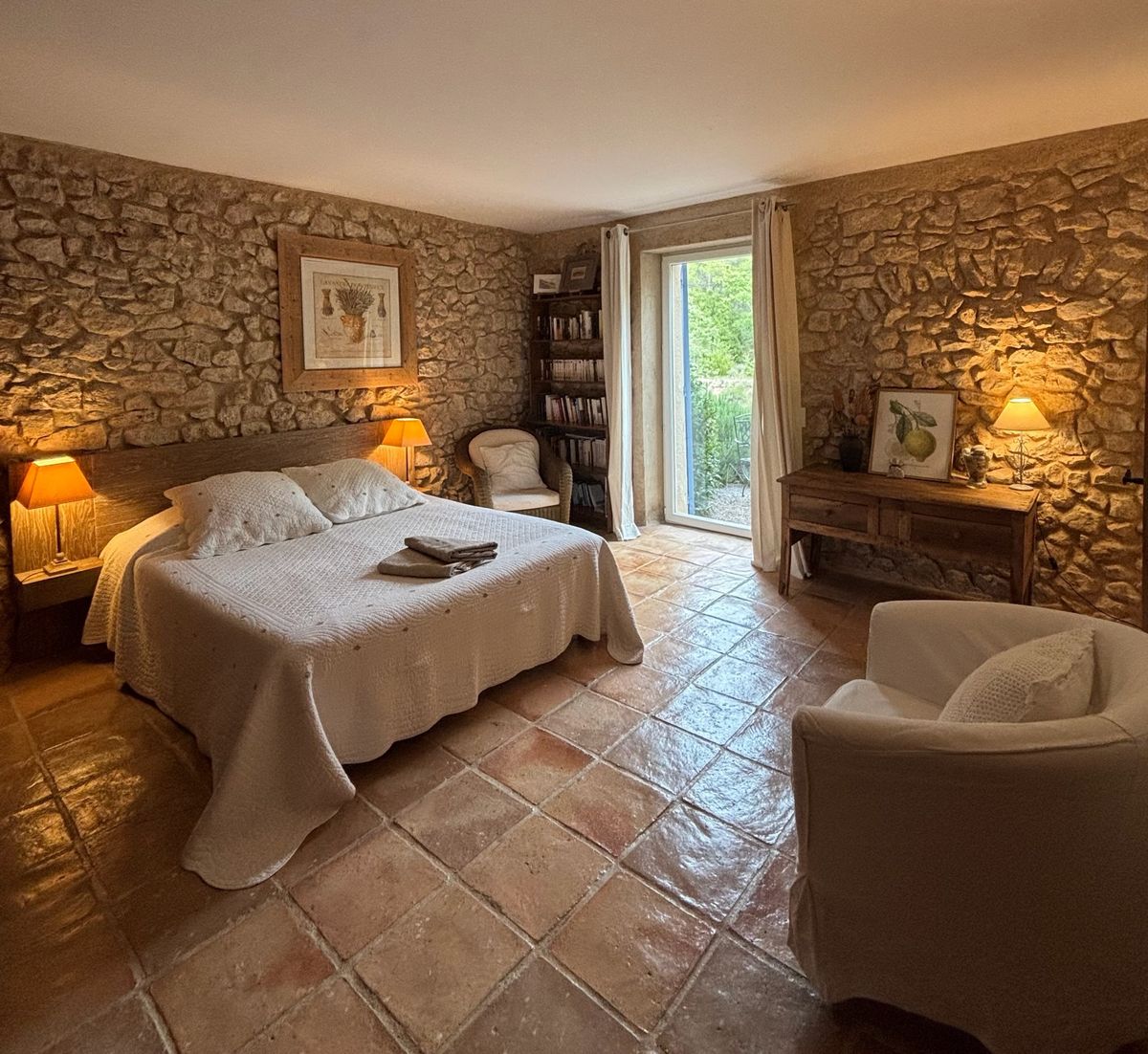 Room 4: double bed between two stone walls, armchair, bookcase and a French window onto the garden.