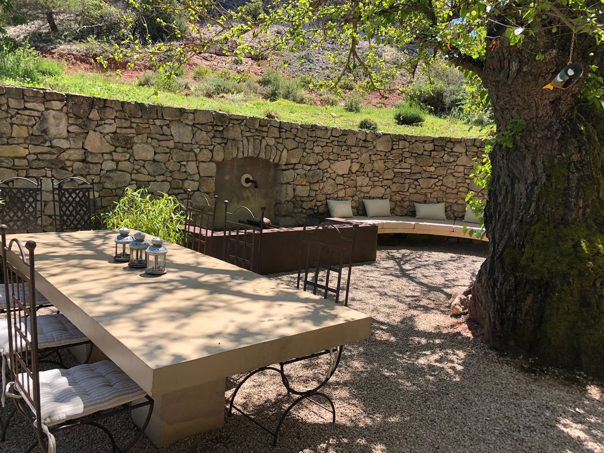 The courtyard: the stone table for twelve in the shade of the mulberry tree, with the fountain and the bench against the dry-stone wall.