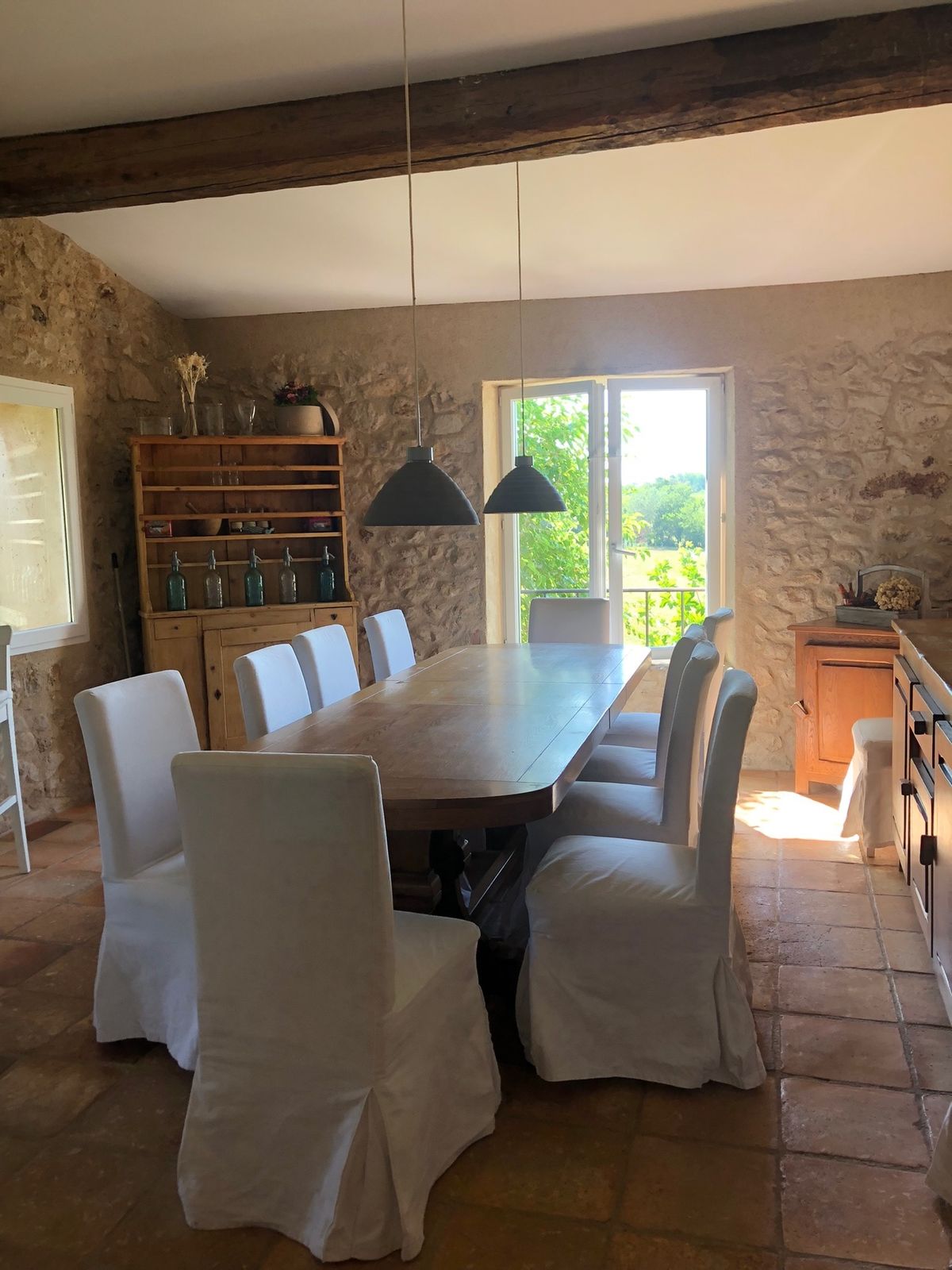 The dining room: a long table with white slip-covered chairs, facing a French window onto the greenery.