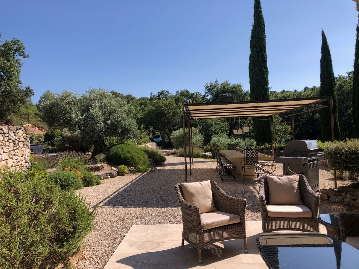 The outdoor sitting area: woven armchairs and a low table, with the pergola and barbecue beyond.