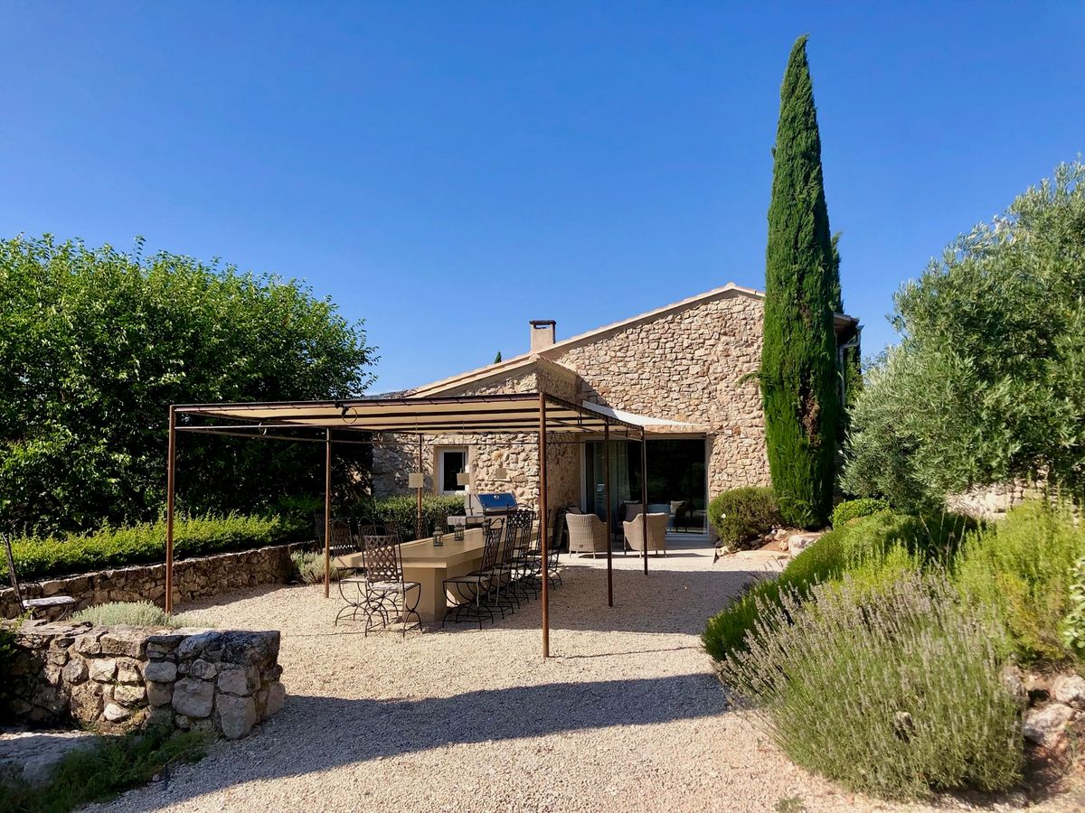 La façade sud : la tonnelle et sa longue table, le salon sous pergola, un grand cyprès et les lavandes.